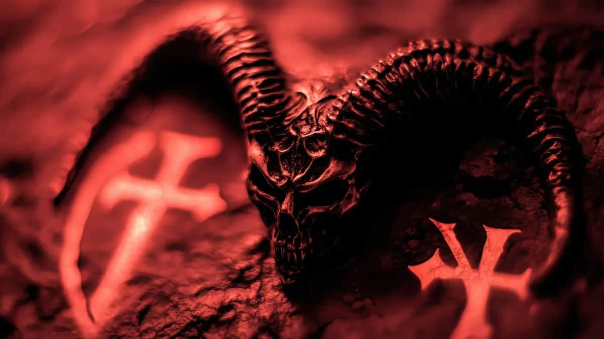 Immagine di un teschio demoniaco con corna e simboli ritualistici illuminati da una luce rossa intensa, evocativa di temi occultistici e atmosfere sataniche.