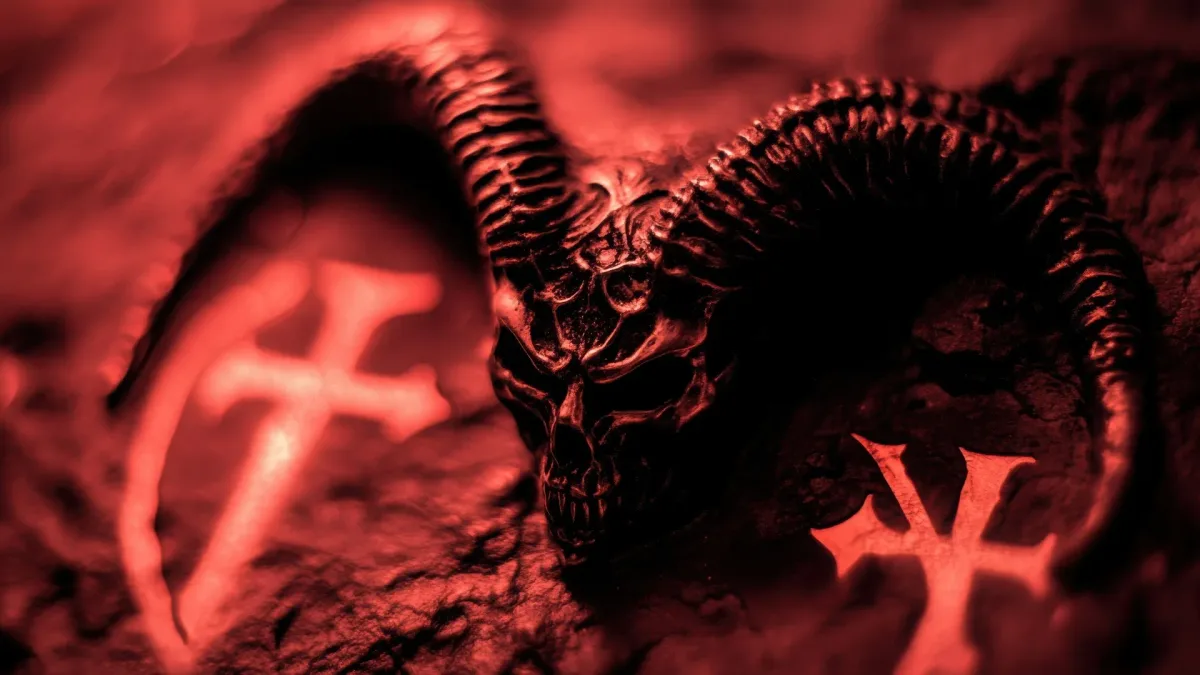 Immagine di un teschio demoniaco con corna e simboli ritualistici illuminati da una luce rossa intensa, evocativa di temi occultistici e atmosfere sataniche.